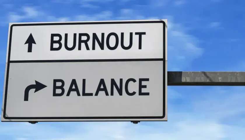 A road sign points to "BURNOUT" straight ahead and "BALANCE" to the right, illustrating the choice between exhaustion and well-being, much like the decision to engage in volunteering.