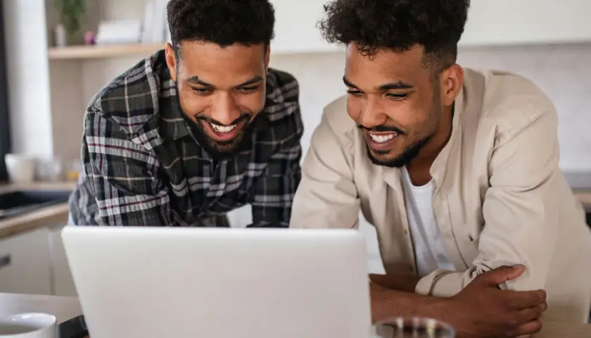 Two men smile at a laptop, possibly reviewing best gofundme examples for their next project.