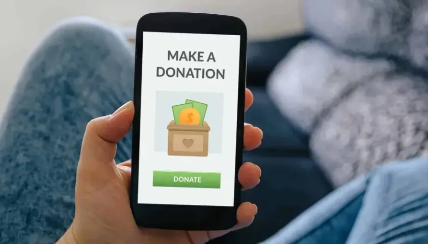 A person uses a donation app on their smartphone, showing a screen with a donation box icon and a "Donate" button.