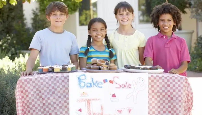 Four kids at a bake sale table, showcasing delicious cupcakes and brownies. Great fundraising ideas for 14 year olds!