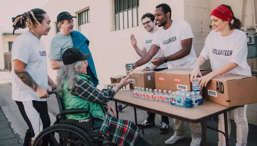 Homeless shelter volunteers hand out water and food to a person in a wheelchair.