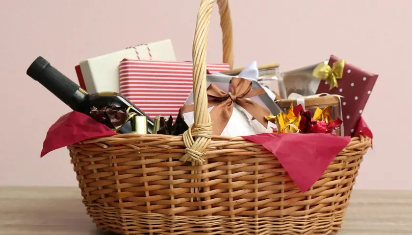A wicker basket filled with gifts, including a bottle of wine, chocolates, and wrapped presents, perfect for cheap raffle prize ideas.