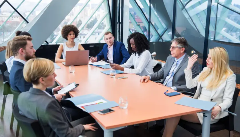 A diverse group of professionals engage in a board meeting, discussing strategy around a large table.