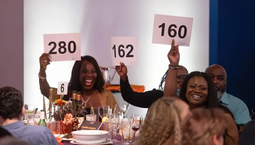 Excited guests participate in a paddle raise fundraiser, holding up signs with numbers like 280, 162, and 160.