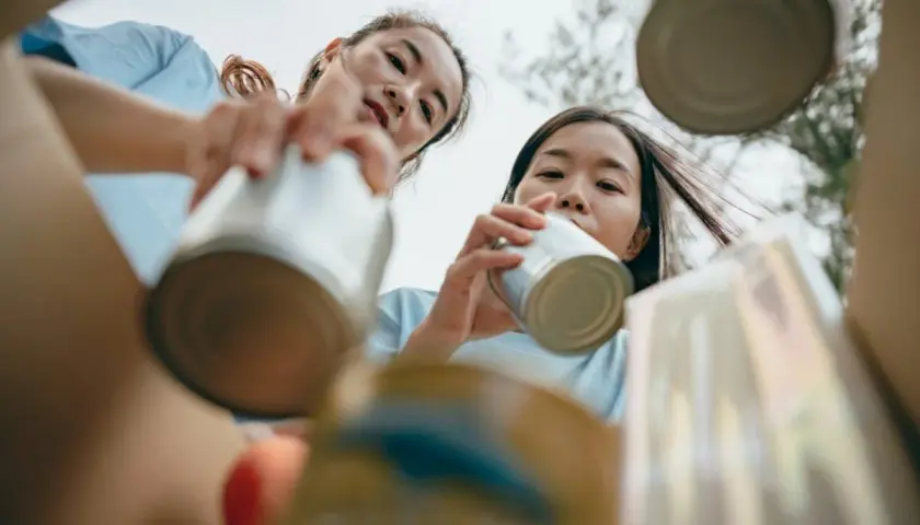 Two young women participate in DEI volunteer opportunities, sorting cans for recycling.