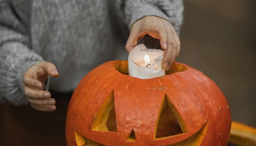 Hands place a lit candle inside a carved pumpkin, a perfect addition to fall festival ideas for work.