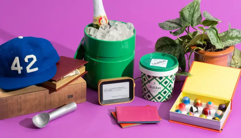 A blue baseball cap with "42" on it, books, a green ice bucket with a bottle, Maldon salt, an e-reader, a passport holder, and a box of chocolates. Small prize ideas for adults.