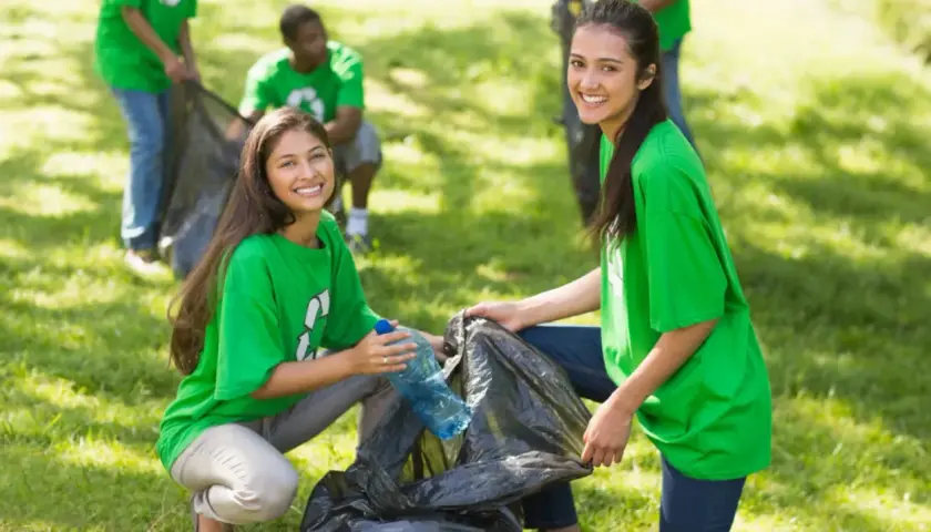 Students participate in community service projects, cleaning up a park and smiling as they collect trash.