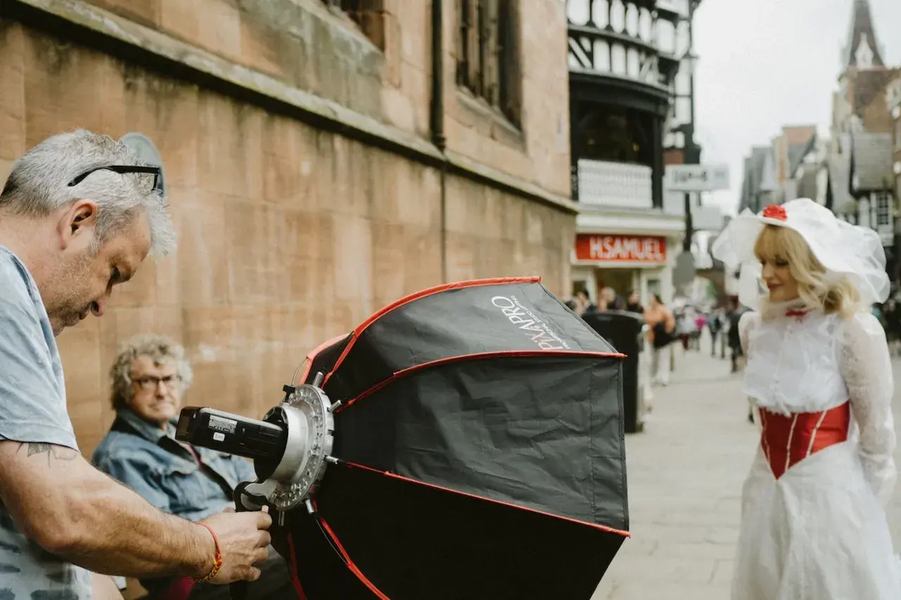A photographer sets up equipment for a photography fundraiser. A woman in a white and red costume stands in the background.