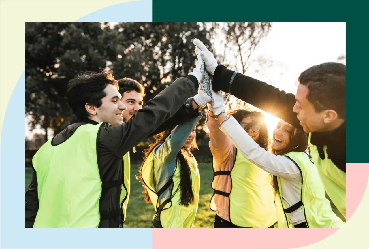 A diverse group of young people in bright vests high-five, celebrating their success in volunteer programs for youth.