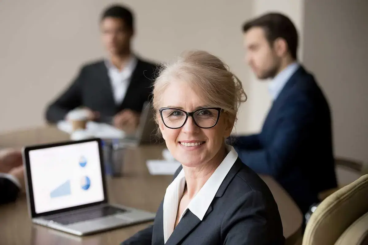 A confident woman leads a board meeting, her laptop displaying charts. This image illustrates how to run a board meeting script effectively.