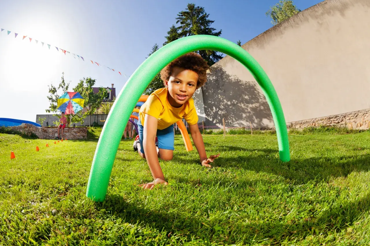 A boy crawls through a green pool noodle arch at a fun elementary school fall festival. Great ideas for outdoor games!