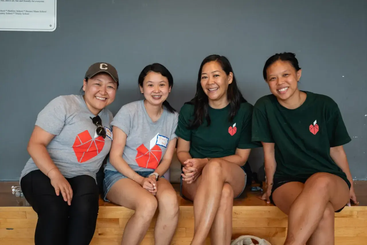 Four smiling women in matching t-shirts with a red heart logo, possibly participating in volunteer opportunities in NYC for college students.