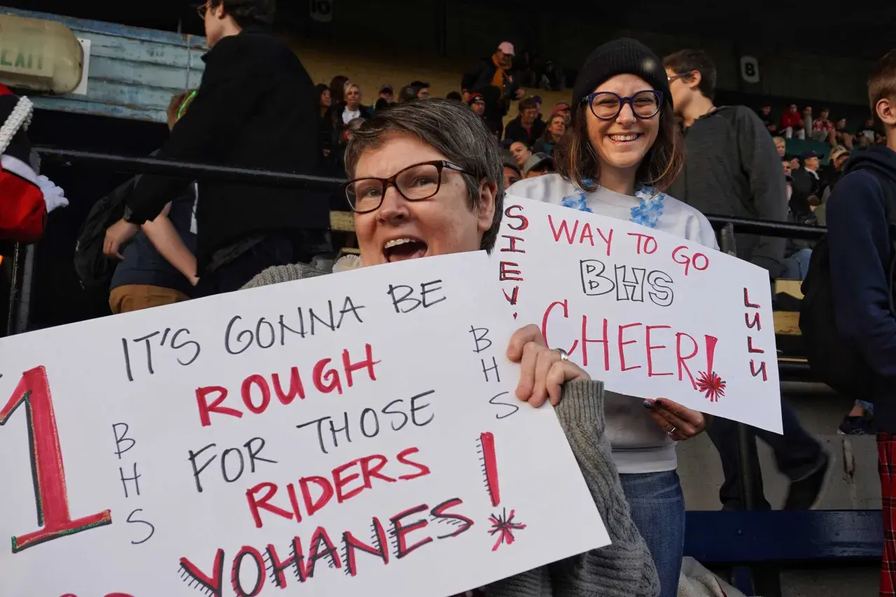 Fans hold signs at a snap raise fundraiser. One sign reads "IT'S GONNA BE ROUGH FOR THOSE RIDERS YOHANES!