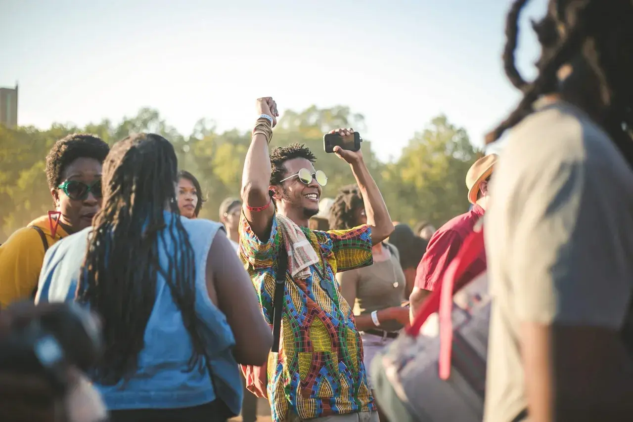 A man with sunglasses and a colorful shirt raises his fist in the air, capturing the energy of a dance-a-thon.