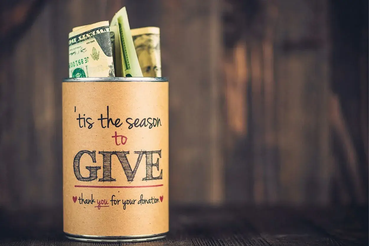 A tin can filled with money, labeled "'tis the season to GIVE," a great example of fundraising sign ideas.