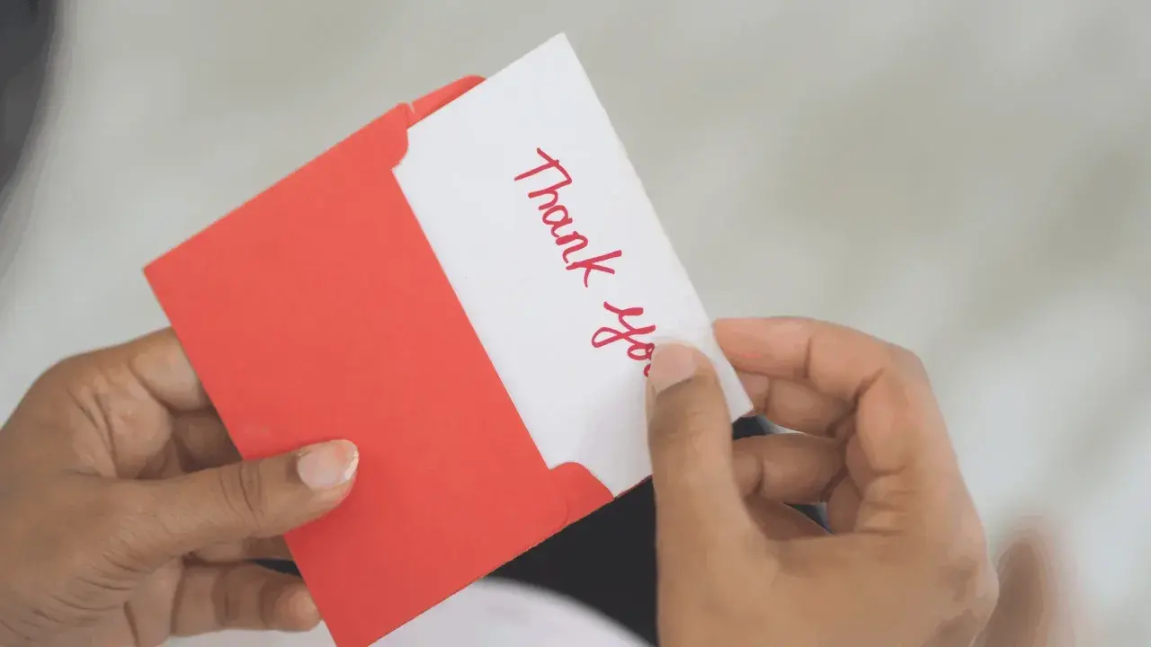 A handwritten "Thank You" card being pulled from a red envelope. A simple yet effective way to show how to reward volunteers.
