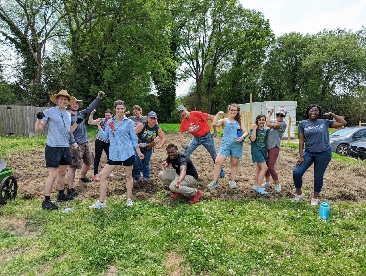 A diverse group of volunteers flexes their muscles, celebrating their hard work on a community service project.