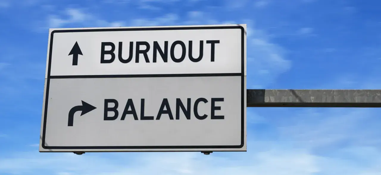 A road sign points to "BURNOUT" straight ahead and "BALANCE" to the right, illustrating the choice between exhaustion and well-being, much like the decision to engage in volunteering.