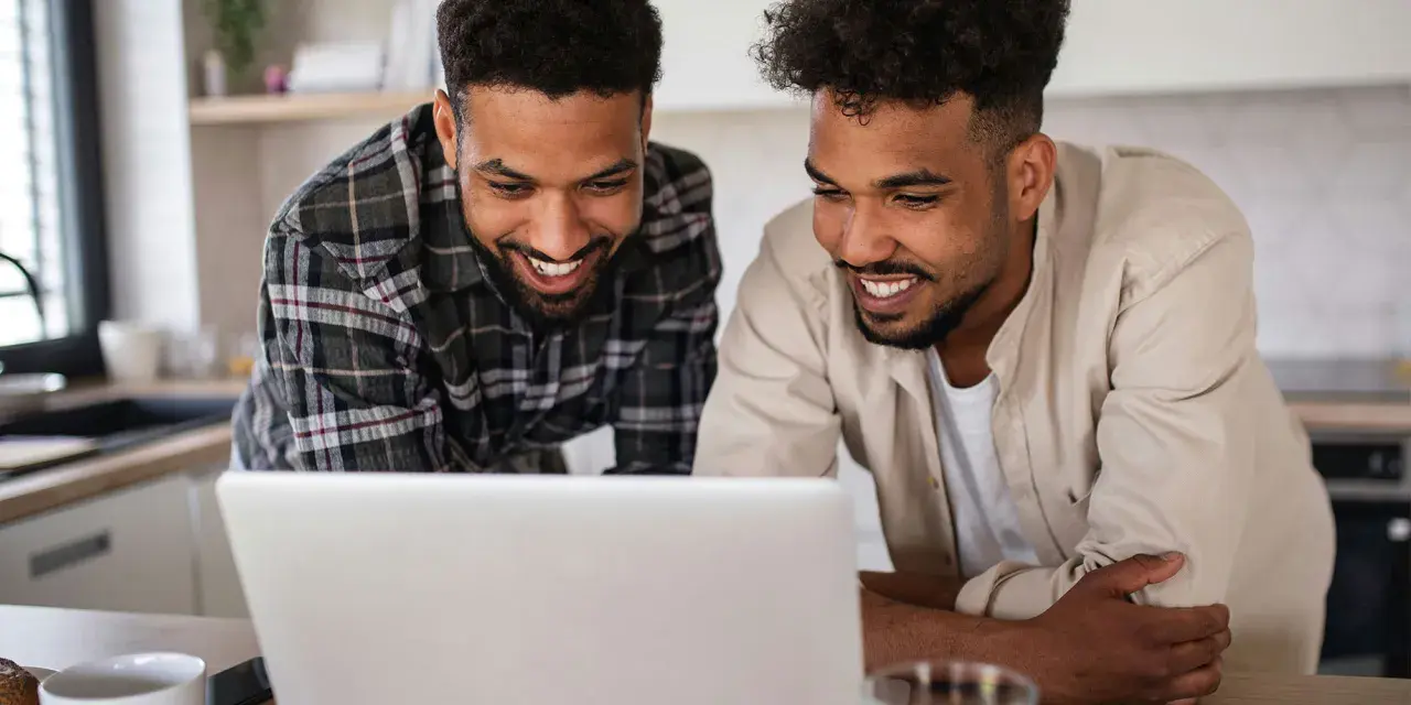 Two men smile at a laptop, possibly reviewing best gofundme examples for their next project.