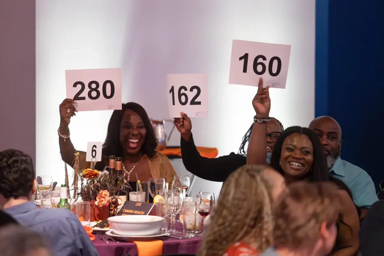 Excited guests participate in a paddle raise fundraiser, holding up signs with numbers like 280, 162, and 160.
