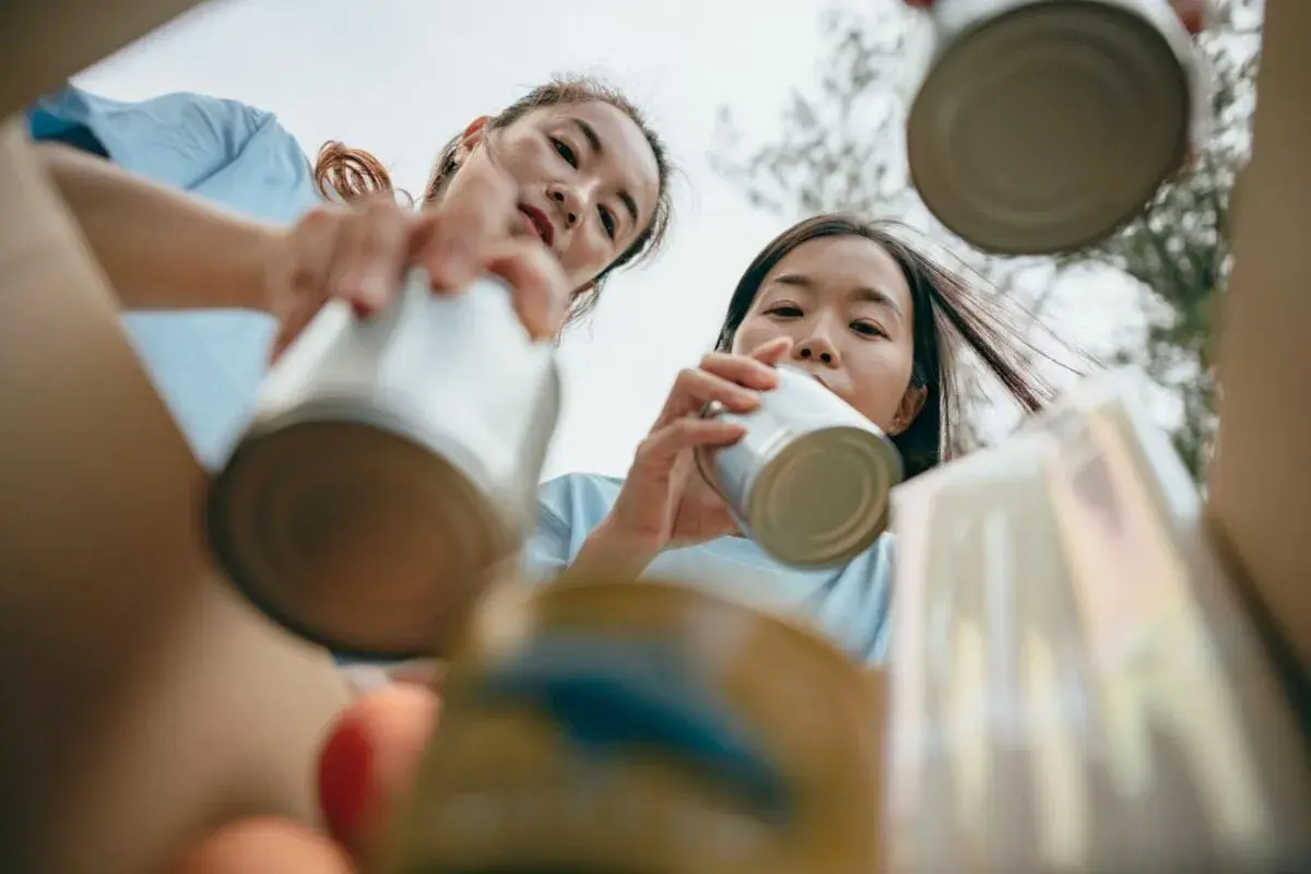Two young women participate in DEI volunteer opportunities, sorting cans for recycling.