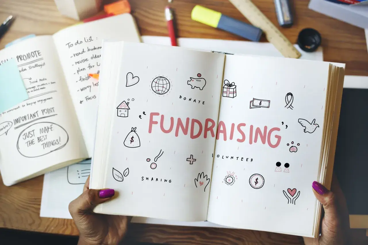 Open notebook with "FUNDRAISING" and icons for easy fundraisers. A to-do list and "Just Make the Best Things!" are visible.
