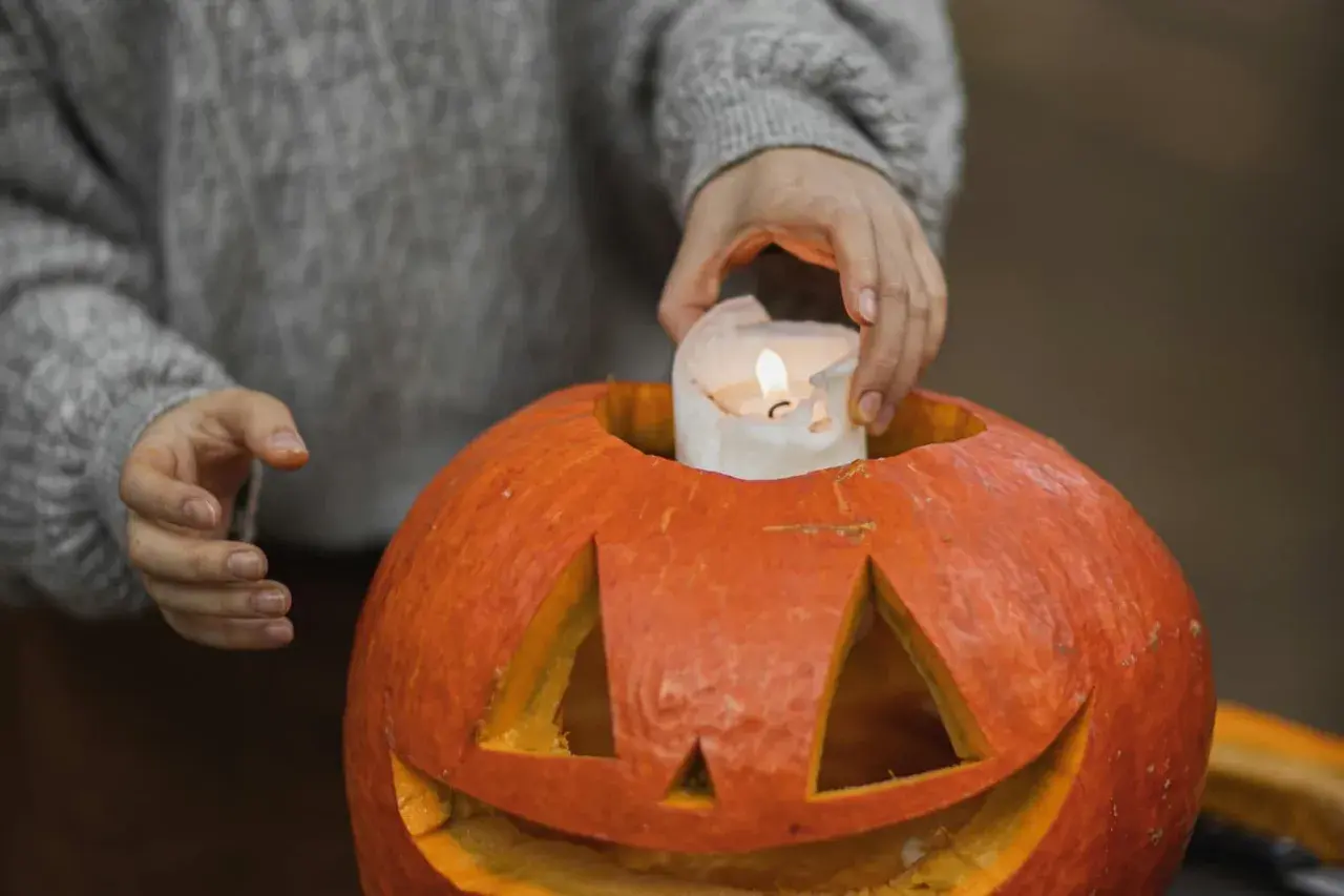 Hands place a lit candle inside a carved pumpkin, a perfect addition to fall festival ideas for work.