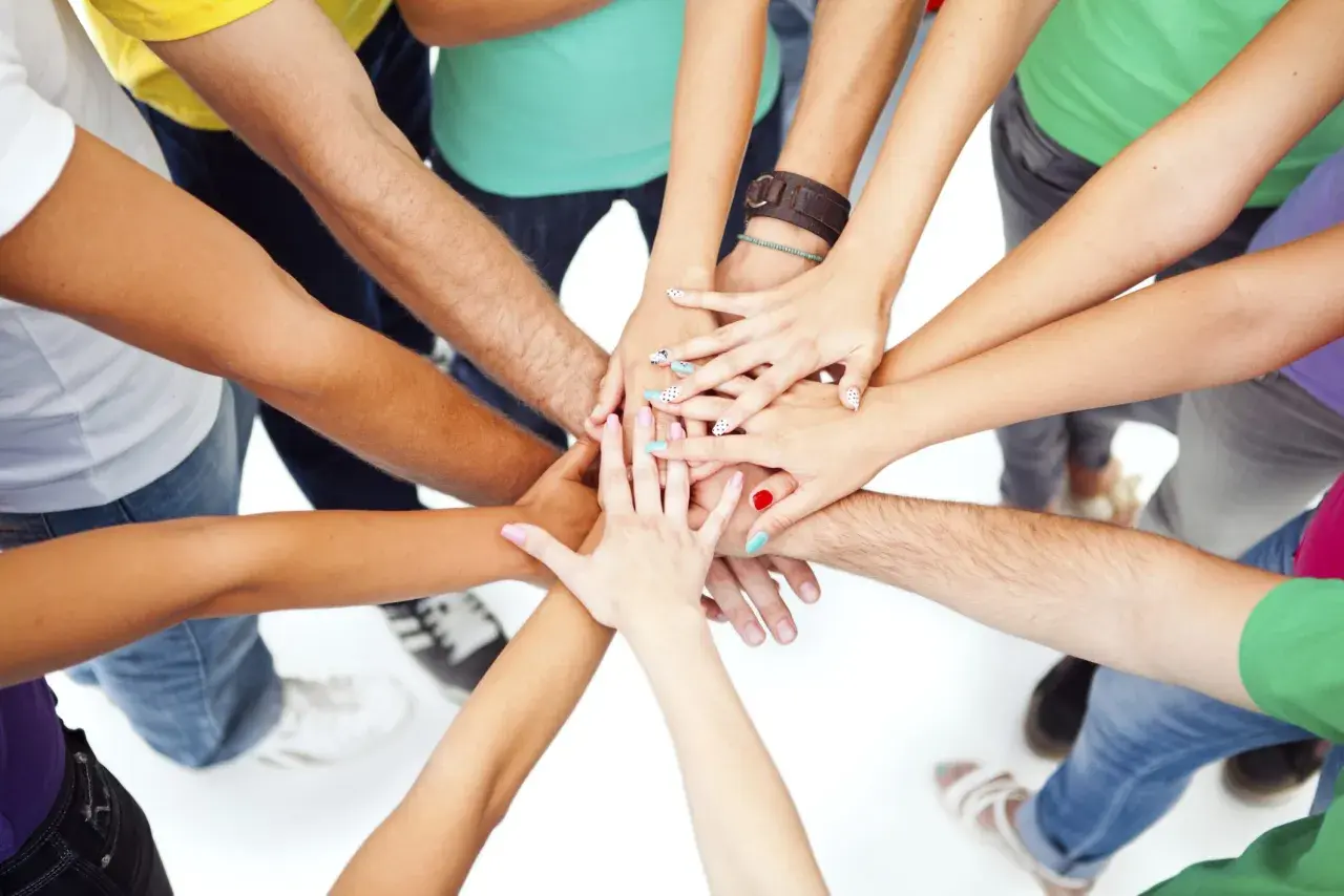 A diverse group of people with colorful nails and bracelets join hands in a circle, symbolizing unity and the spirit of a service trip.