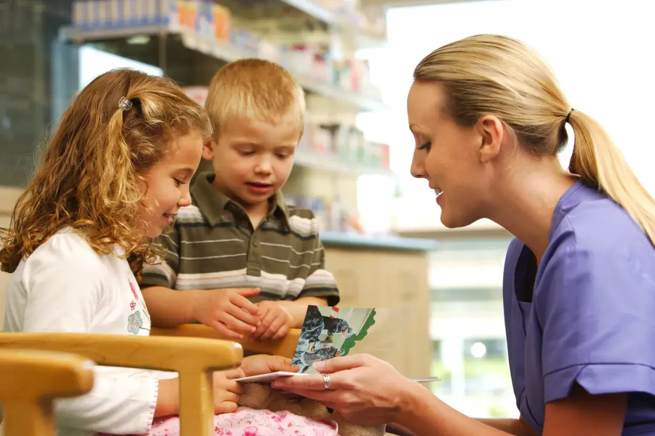 A Kaiser Permanente volunteer program member reads a book to two children in a bright, clean setting.