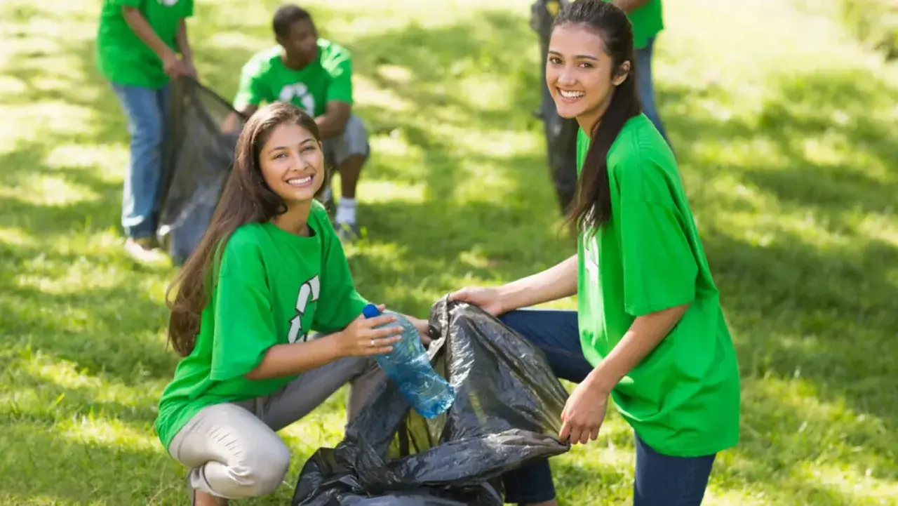 Students participate in community service projects, cleaning up a park and smiling as they collect trash.