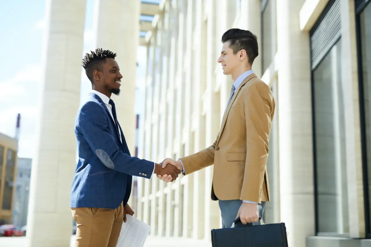 Two businessmen shake hands outside a modern building, perhaps after a successful meeting facilitated by their board portal.