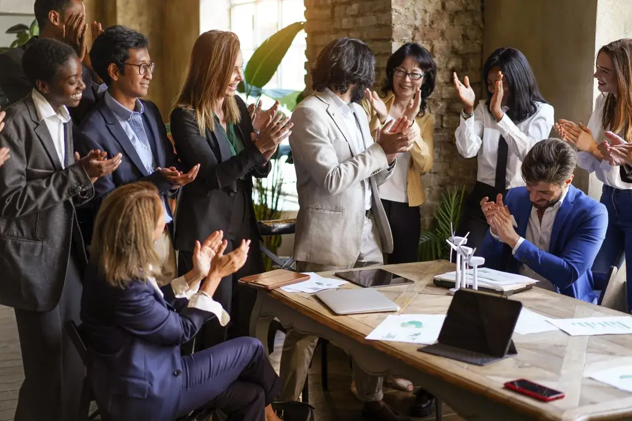 A diverse team applauds, celebrating a successful board fundraising initiative. Their smiles and clapping hands convey a shared sense of accomplishment.