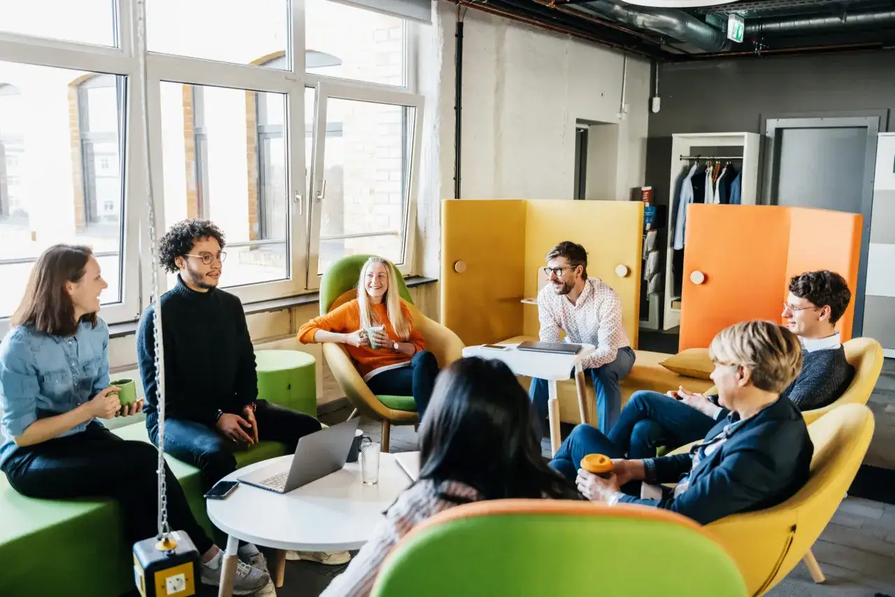 A diverse group of people are gathered in a modern office space, discussing plans to organize volunteers for an upcoming event.