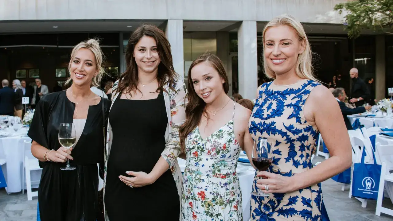 Four women pose at a photography fundraiser event, smiling and holding drinks.