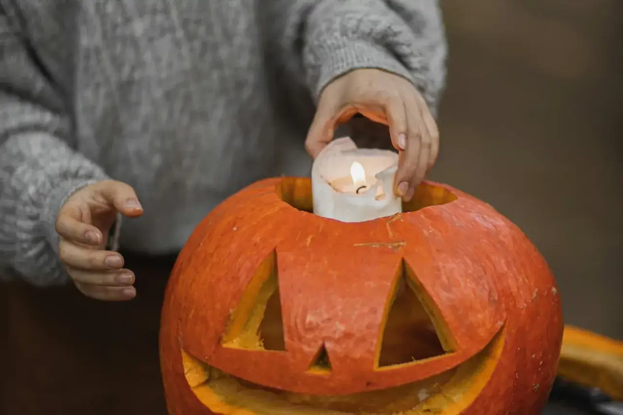 Hands place a lit candle inside a carved pumpkin, a perfect addition to fall festival ideas for work.