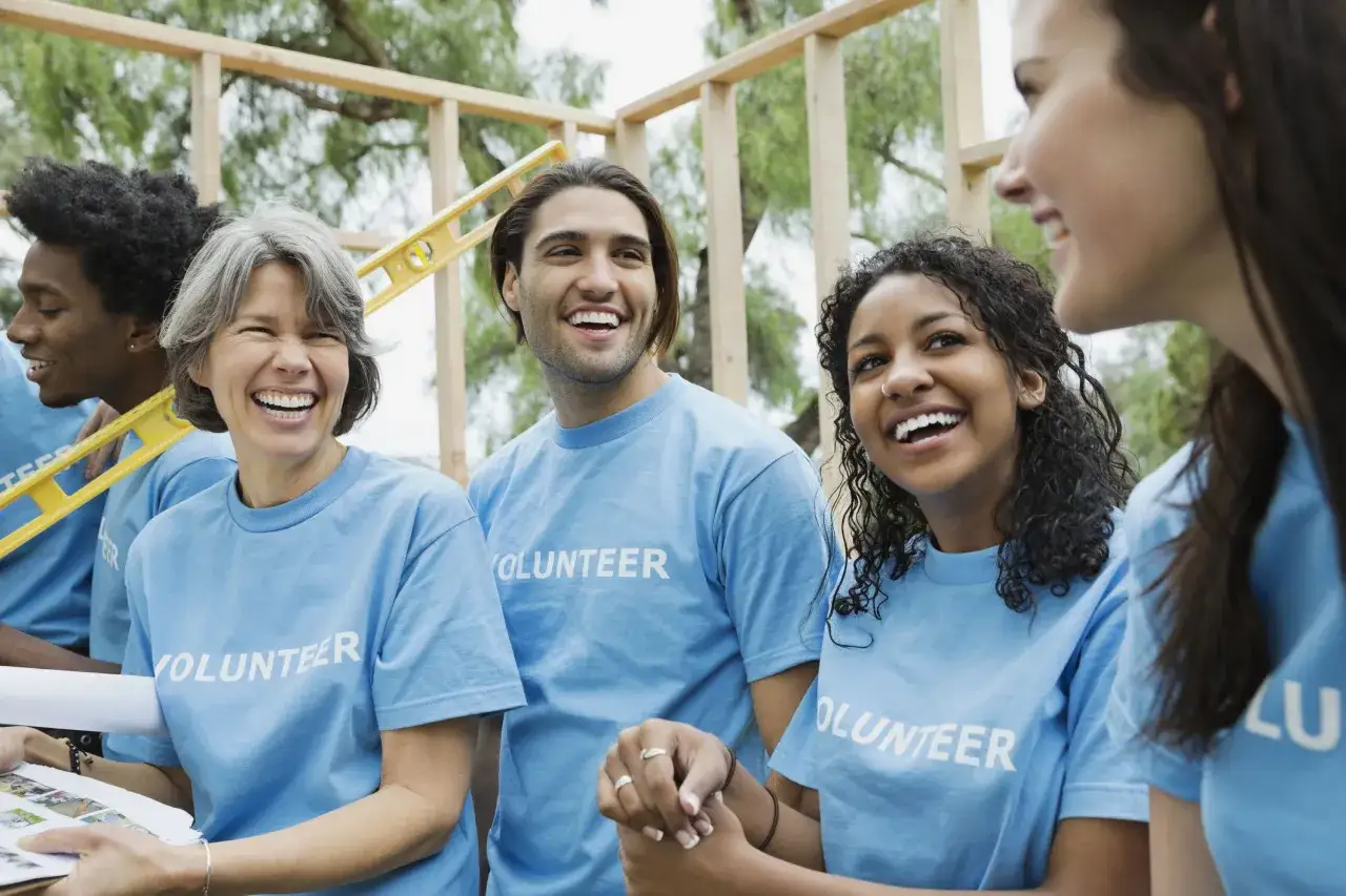 Volunteers in blue shirts laugh while working on a construction project, brainstorming ideas for fundraisers for nonprofit organizations.