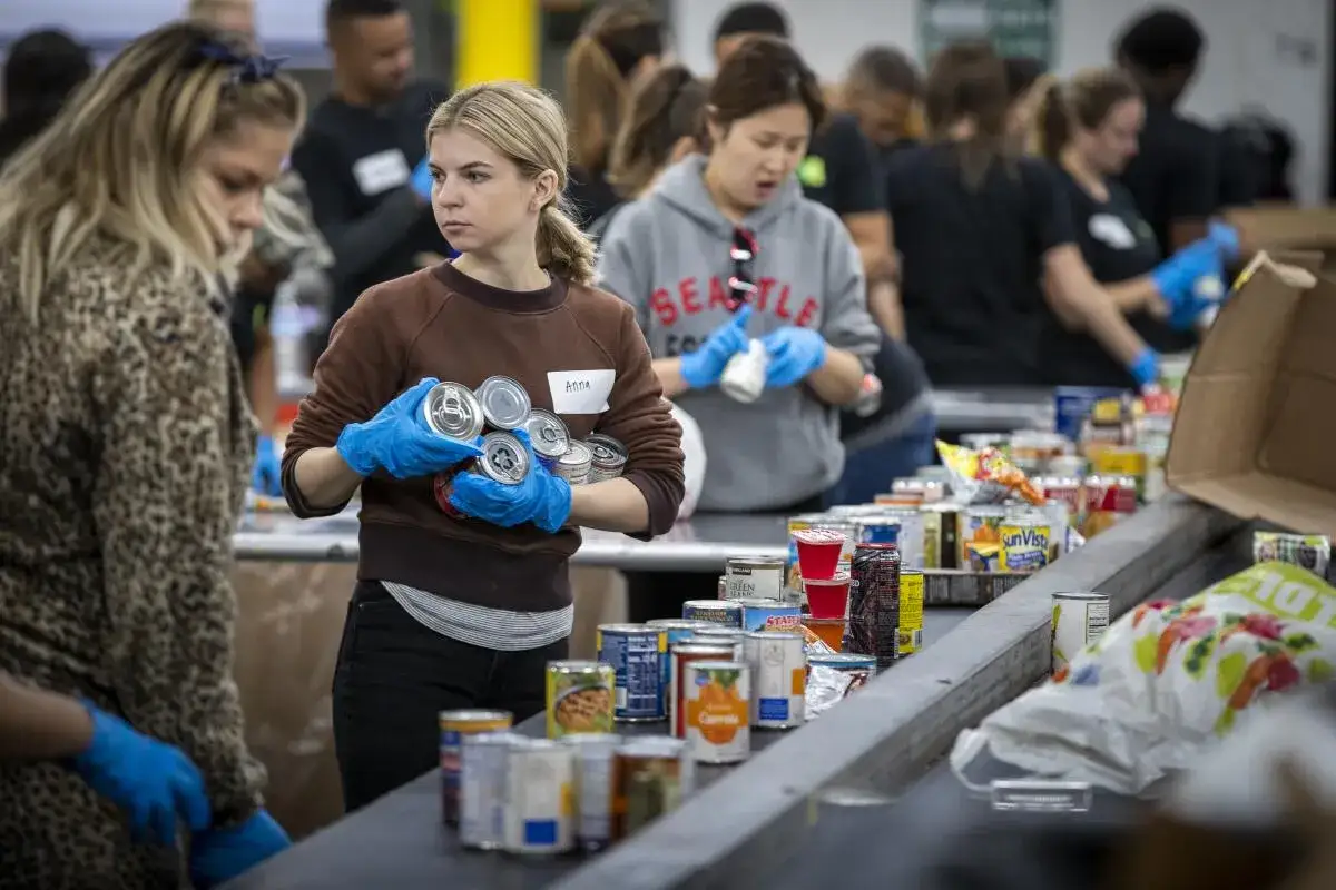 Anna, a student volunteer, sorts canned goods at a food bank. Other volunteers work in the background.