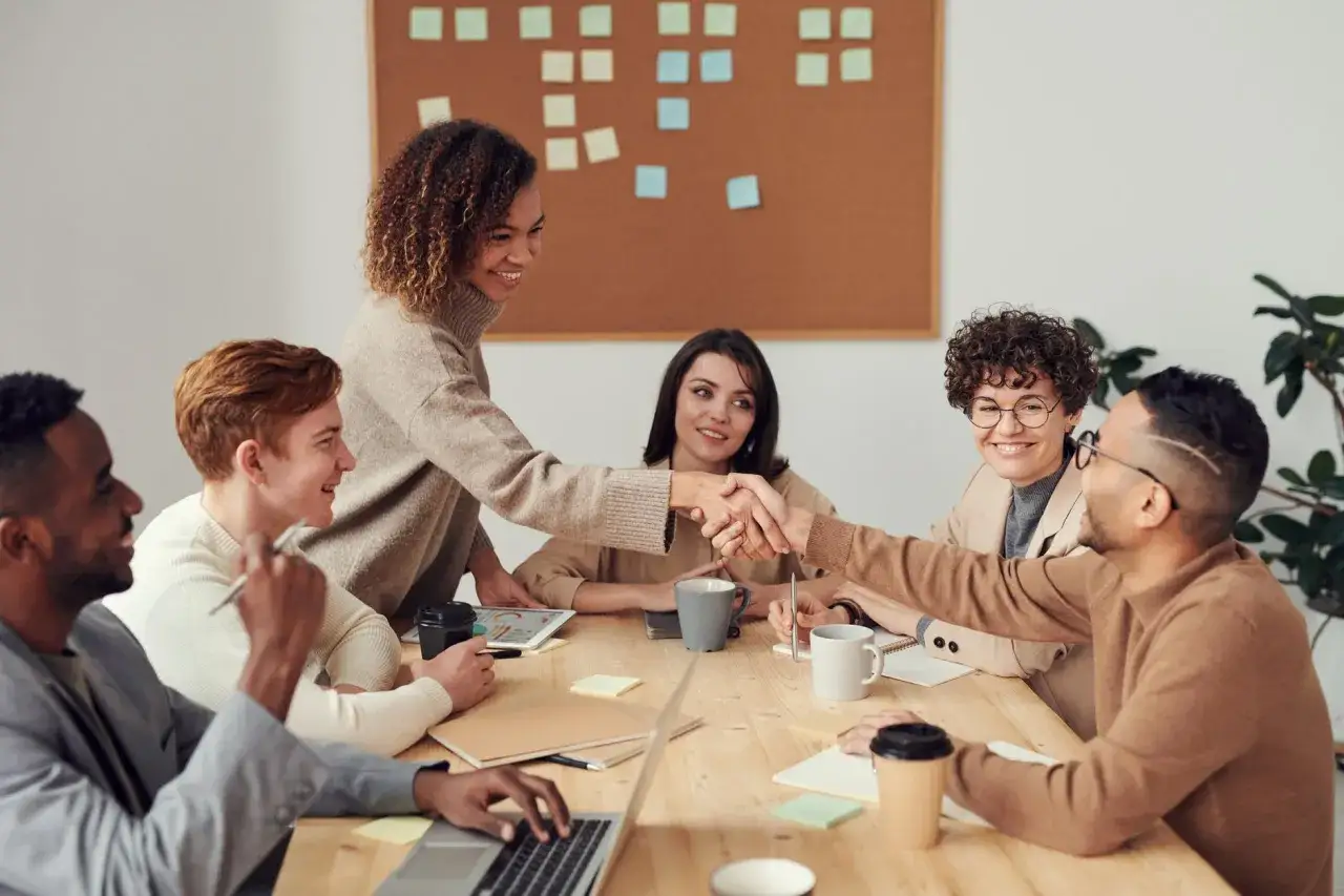 A diverse team collaborates, with two members shaking hands, symbolizing agreement on governance team roles and responsibilities.