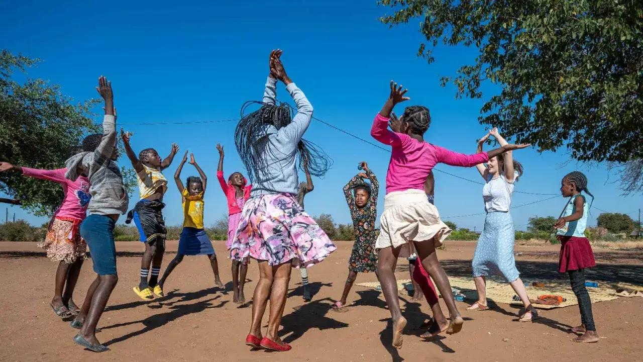 Children joyfully participate in voluntary community service, dancing and playing outdoors under a clear blue sky.