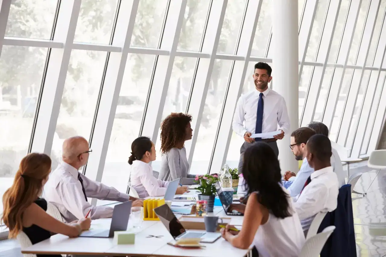 A diverse group of professionals, likely the nominating and governance committee, are in a meeting around a table, with a presenter standing.