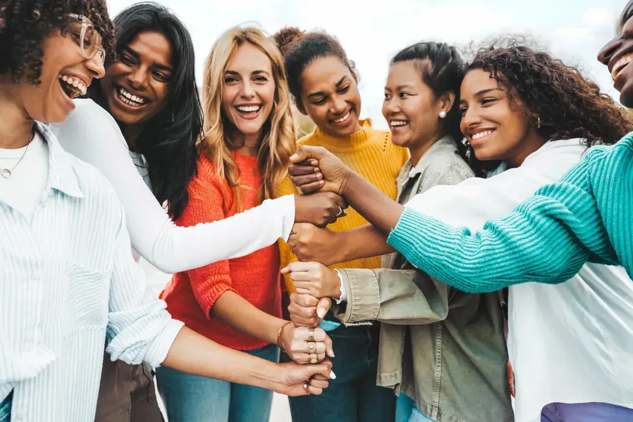 Diverse women share laughter and a fist bump, symbolizing overcoming volunteering problems through unity and collaboration.