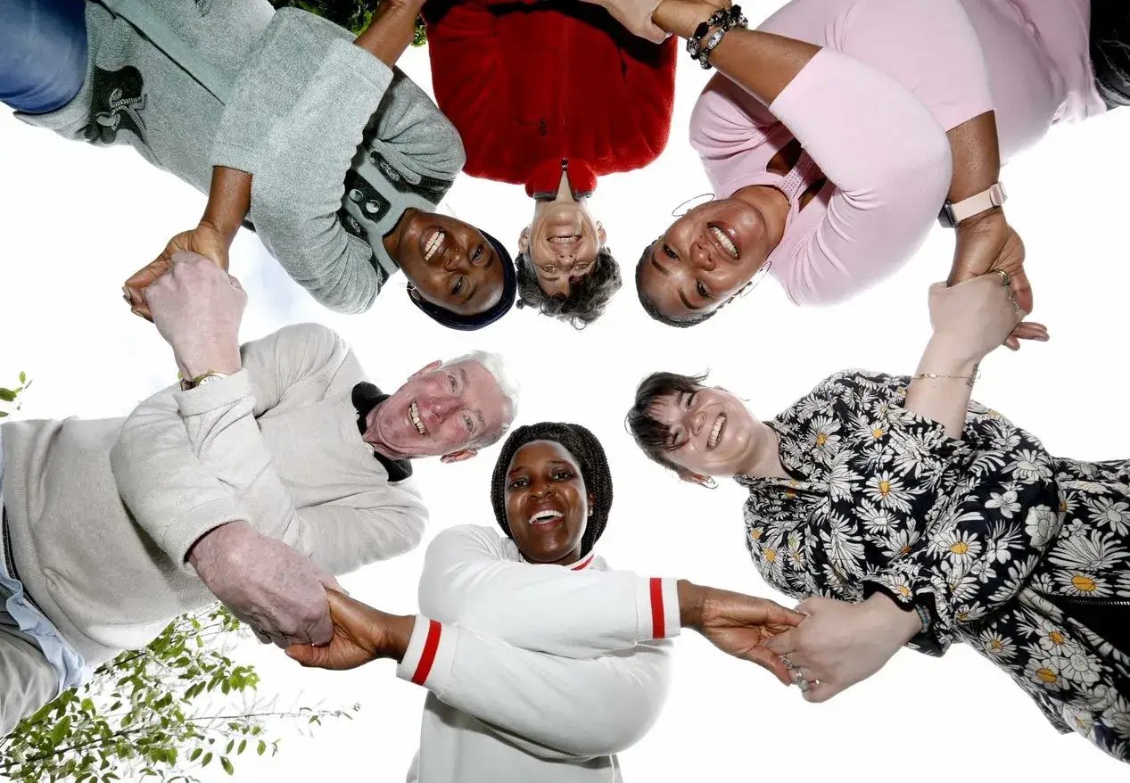 Diverse group of people holding hands in a circle, smiling. They represent many ways to volunteer and connect with others.