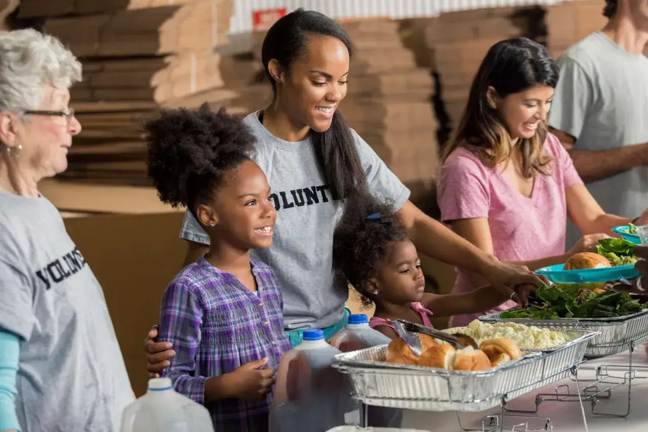 Volunteers, including children, serve food at a community event. This image shows great places for kids to volunteer and help others.