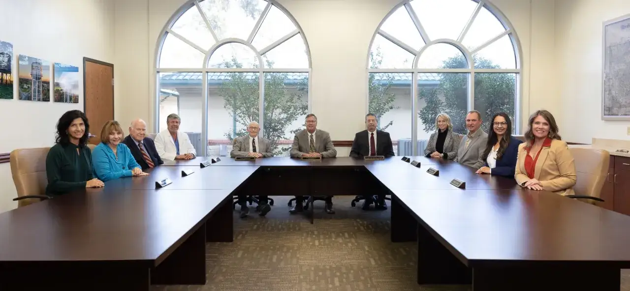 A diverse group of 10 people sit around a U-shaped table in a boardroom. The question of whether hospital board members get paid is often complex, with compensation varying by institution.