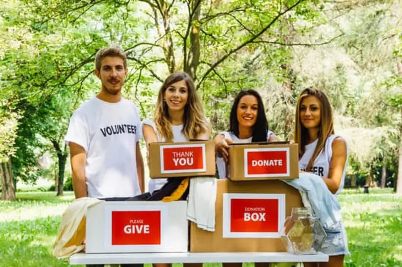 Volunteers stand behind donation boxes, showcasing great donation drive ideas. One box says 