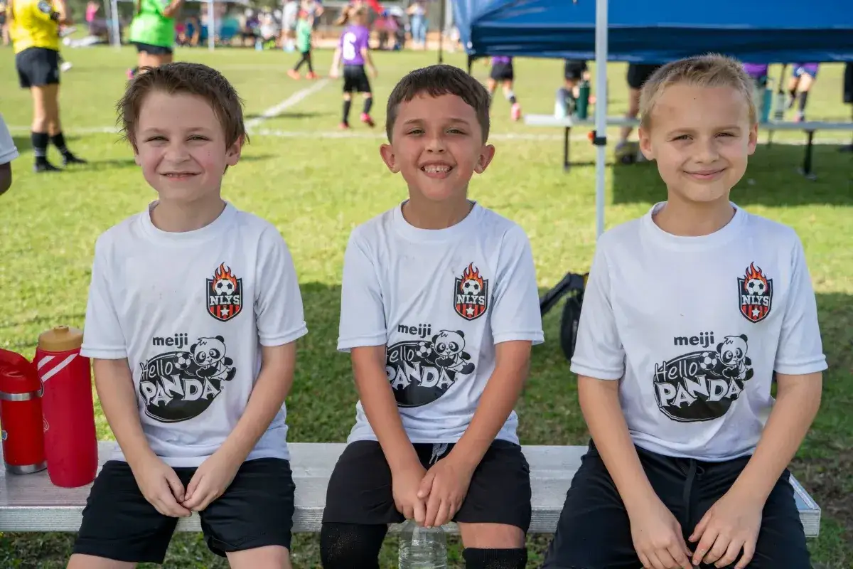 Three smiling boys in soccer jerseys pose for a photo at a soccer fundraiser.