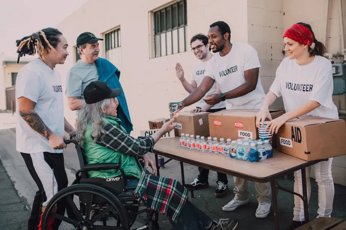 Homeless shelter volunteers hand out water and food to a person in a wheelchair.