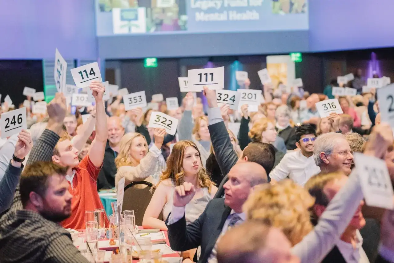 Attendees at a paddle raise fundraiser enthusiastically hold up numbered paddles, bidding for a cause.