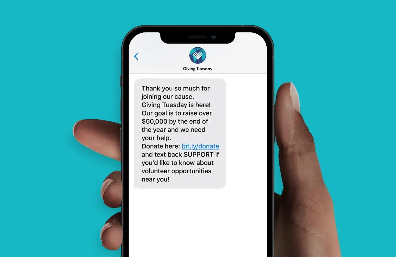 A phone displays a text message for Giving Tuesday, thanking the recipient and asking for donations or volunteer support.